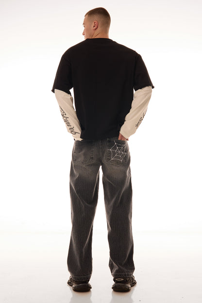 Model văzut din spate purtând tricoul DUAL LONG TEE Skyweb, tricou negru cu mâneci albe layered și print pe mâneci.