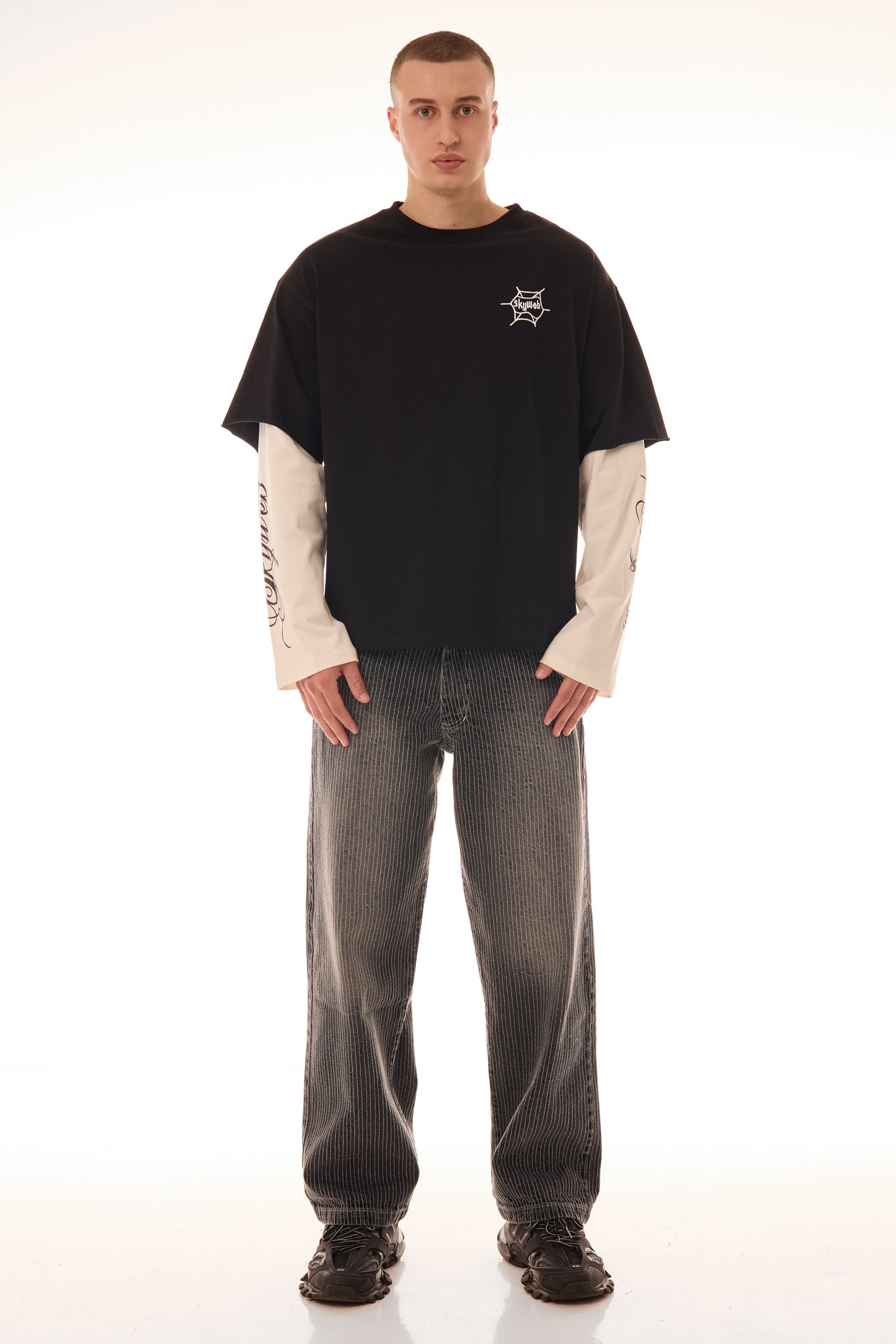 Model purtând tricoul DUAL LONG TEE Skyweb, tricou negru cu mâneci albe layered și print pe piept – vedere frontală.