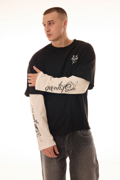 Model în poziție 3/4 purtând tricoul DUAL LONG TEE Skyweb, tricou negru cu mâneci albe layered și print gotic pe mâneci.