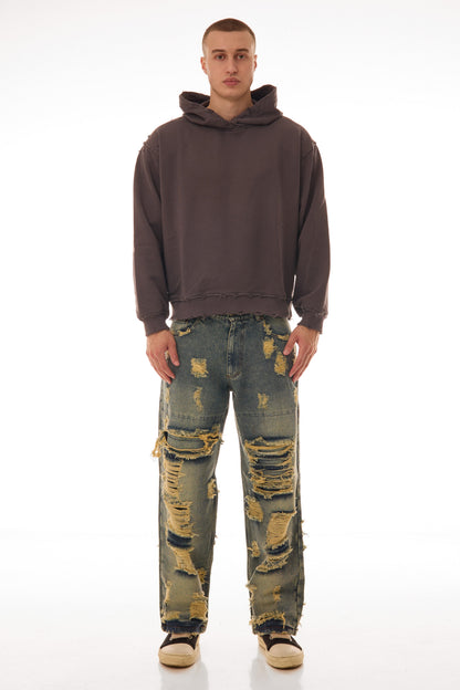 Model purtând blugii Shattered Denim Blue 13.5 OZ, wide fit, cu distressed heavy și rupturi mari pe partea frontală.
