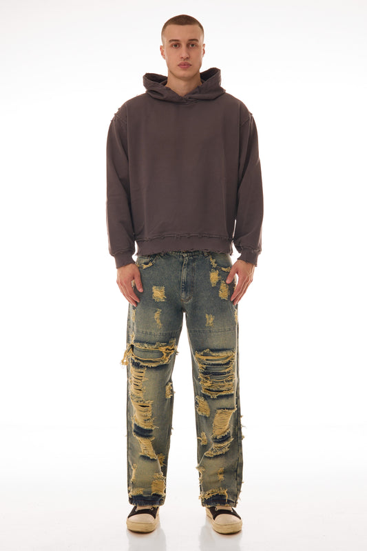 Model purtând blugii Shattered Denim Blue 13.5 OZ, wide fit, cu distressed heavy și rupturi mari pe partea frontală.
